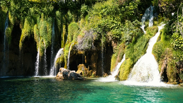 Real Plitvice Lakes waterfalls flowing into a turquoise forest pool